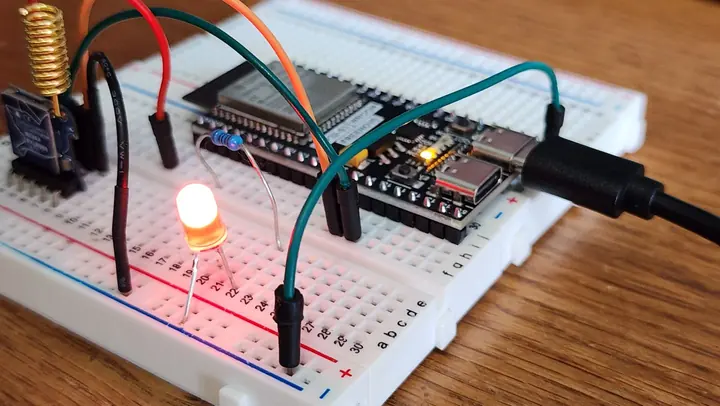 Protoboard e placa de microcontrolador sobre uma bancada de madeira, com LED aceso
