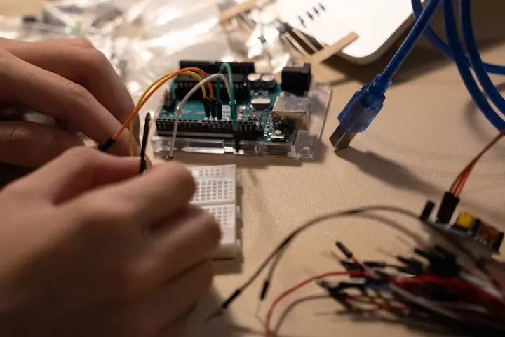 Mãos encaixando um fio jumper na protoboard