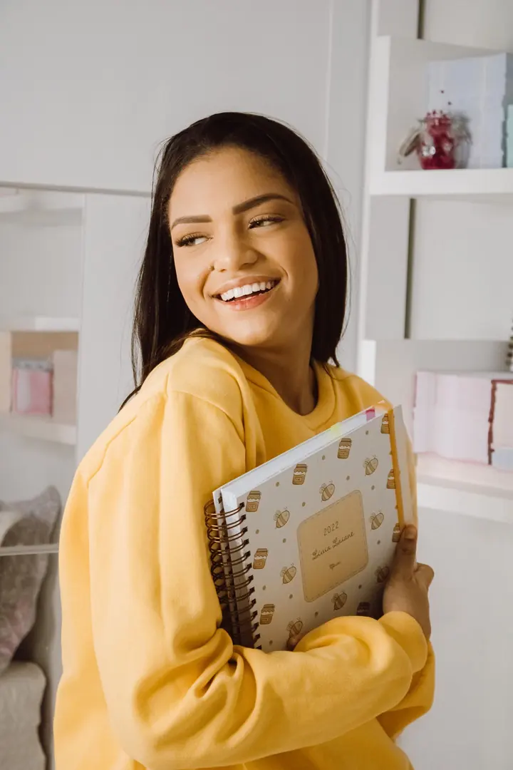 Estudante sorrindo, com um caderno apoiado no braço